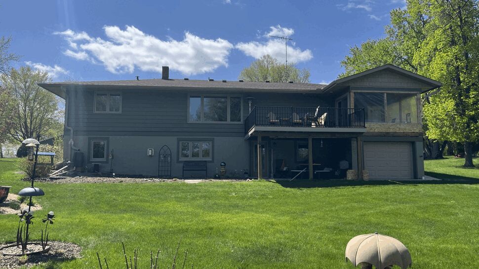 Backyard view of house with large windows and an elevated deck over patio
