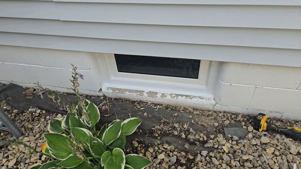 Close-up of a basement window with peeling paint and caulking tools nearby.