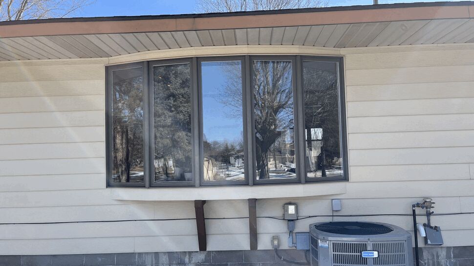 Close-up bay window above an outdoor HVAC unit on beige siding