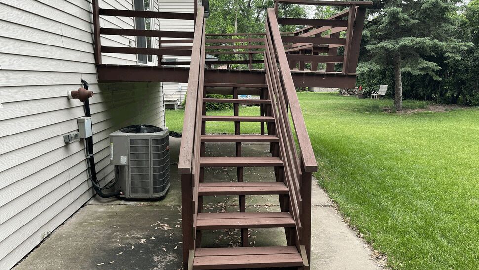 Aging brown-painted wood deck with horizontal railing on a raised ranch home in St. Cloud, MN