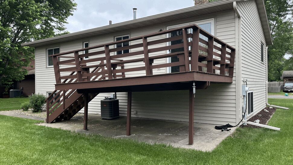 Aging brown-painted wood deck with horizontal railing on a raised ranch home in St. Cloud, MN