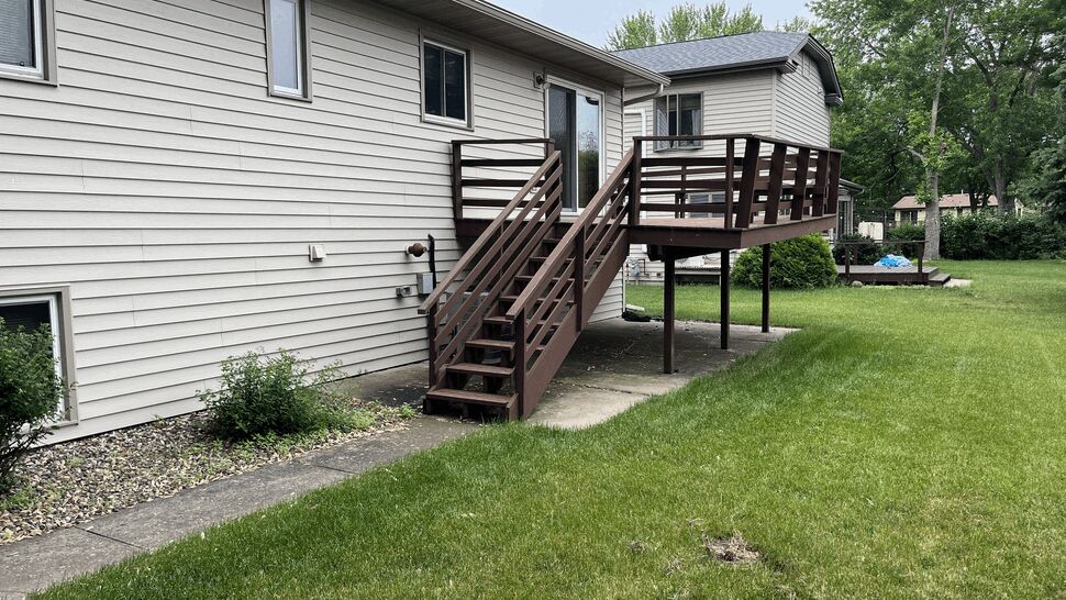 Aging brown-painted wood deck with horizontal railing on a raised ranch home in St. Cloud, MN