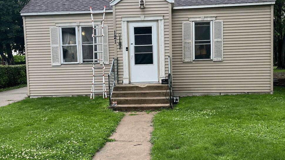 Gutter inspection at bungalow front entry | Lutgen Companies Front of home with ladder against the eave and path leading to door.