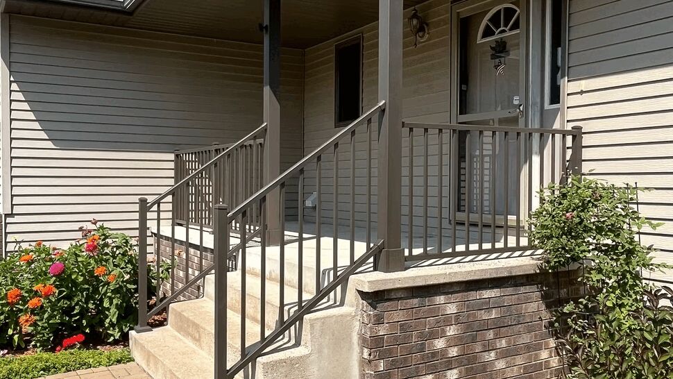 Covered front porch with concrete steps, metal railing and brick knee wall.