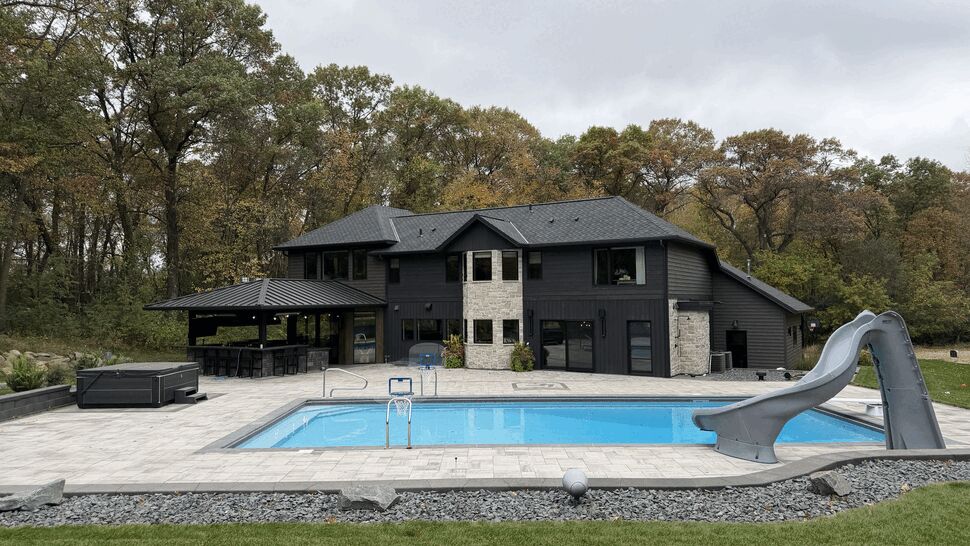 Modern Home with Pool and Outdoor Living | Lutgen Companies Modern dark-sided home with a pool, patio, covered outdoor kitchen, and slide.