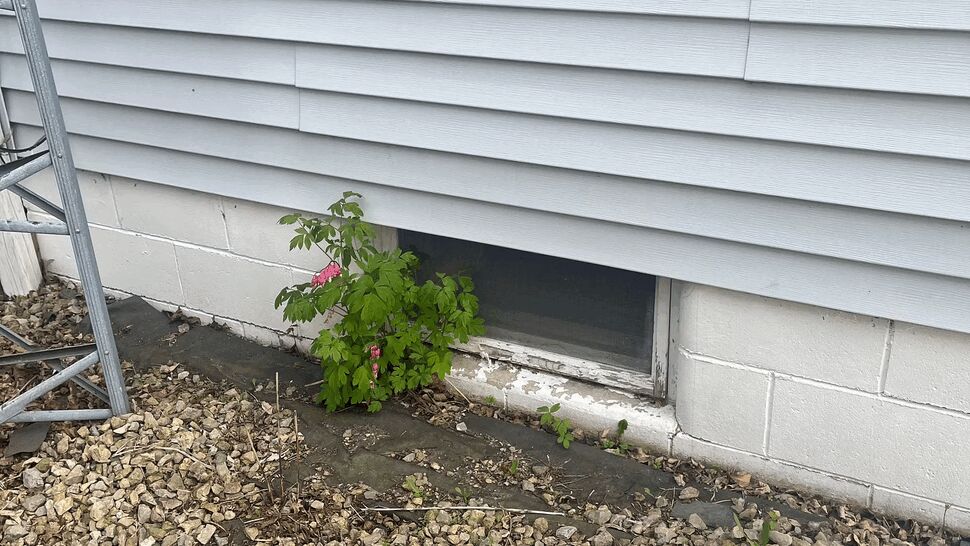 White vinyl siding over block foundation with a small basement window and gravel bed.