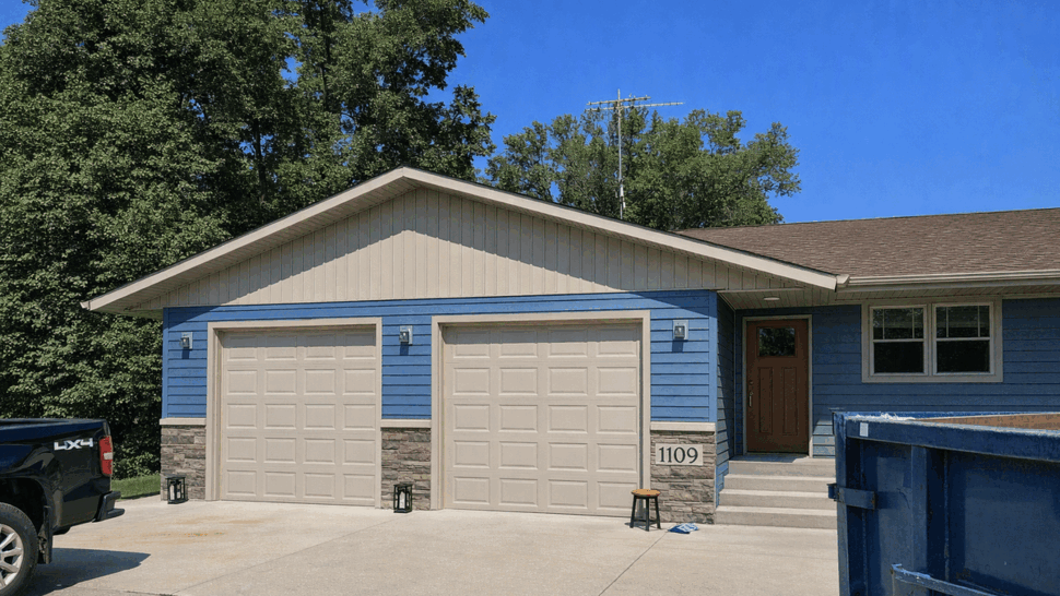 Two-car garage with beige doors and blue siding on the house facade