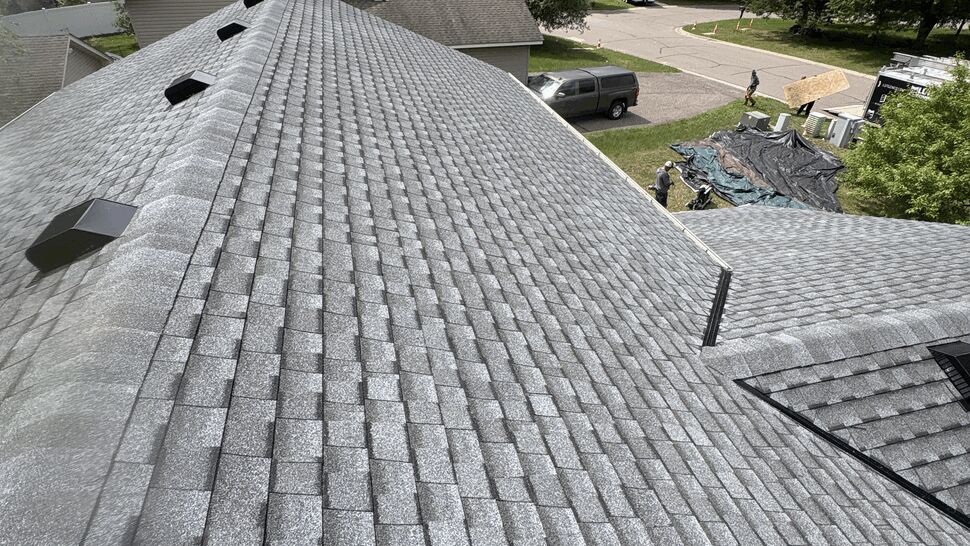 Completed gray asphalt shingle roof | Lutgen Companies Close-up of a new gray GAF Timberline UHDZ shingle roof with ridge cap and roof vents, with the Lutgen crew cleaning up below