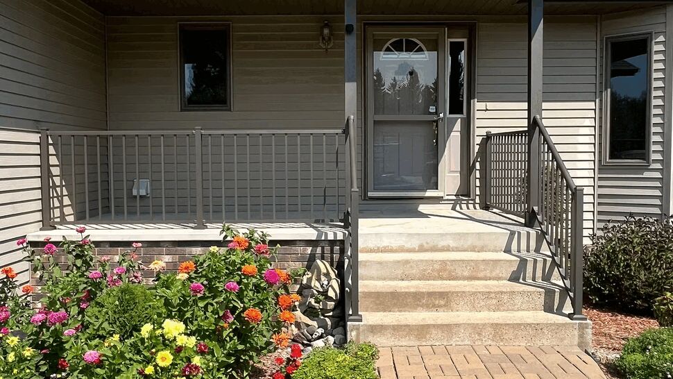Brick paver walkway to porch entrance lined with colorful flower beds and railing.