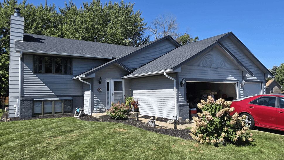Front of gray split-level home with black roof, gutters, and attached garage.