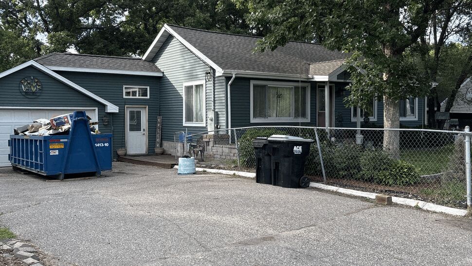Blue-sided home viewed from the driveway with a construction dumpster nearby