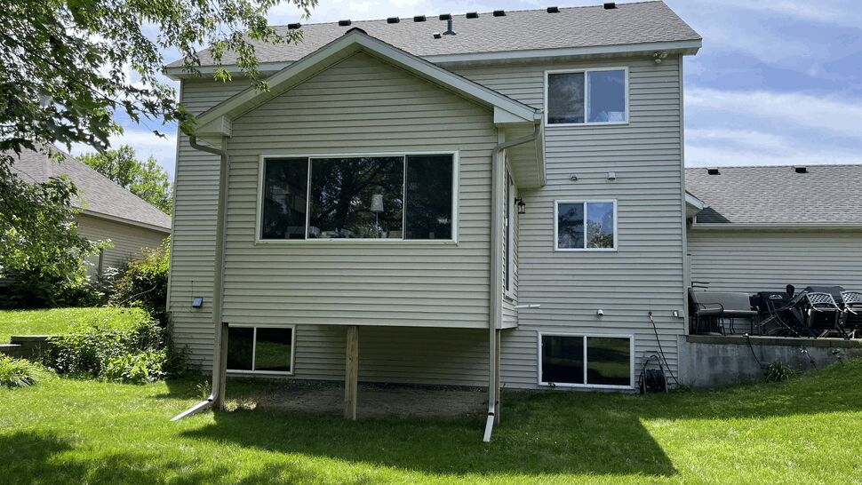 Rear view of a home with light siding, roof, windows, and gutters