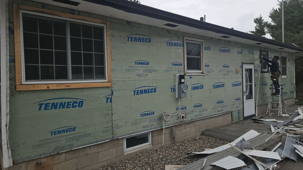 Insulation Installation in Progress | Lutgen Companies Exterior wall with green insulation sheathing and worker on ladder