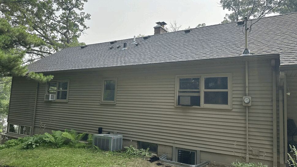Side of house with vinyl siding, roof shingles, windows and metal window wells.