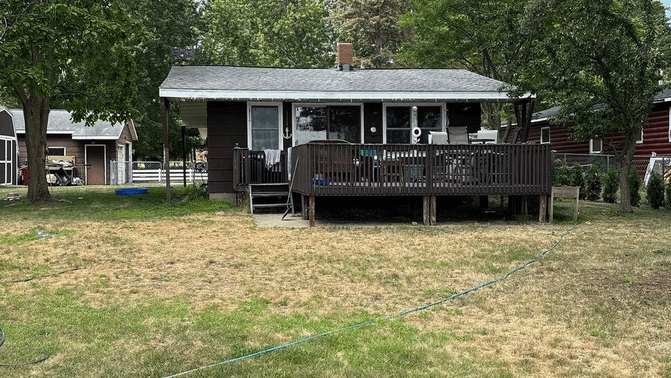 Raised Lakeside Deck with Yard | Lutgen Companies Small brown lakeside house with raised wooden deck and yard