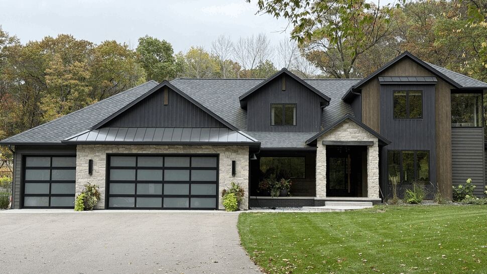 Modern Black Home Exterior | Lutgen Companies Modern black home with gray roof, stone accents, and large windows surrounded by trees.