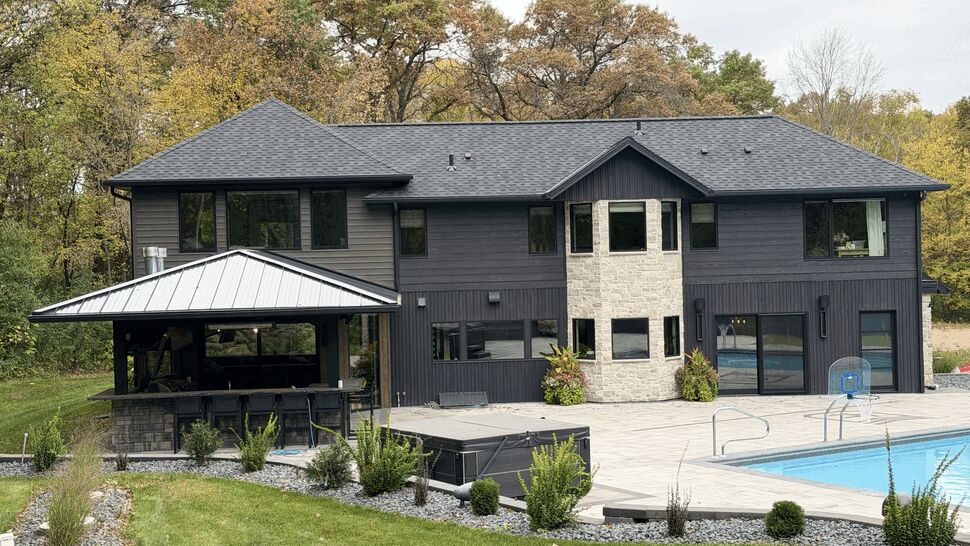 Modern Home Exterior and Pool Patio | Lutgen Companies Modern dark-sided home with stone accents, pool patio, covered outdoor kitchen, and landscaping.