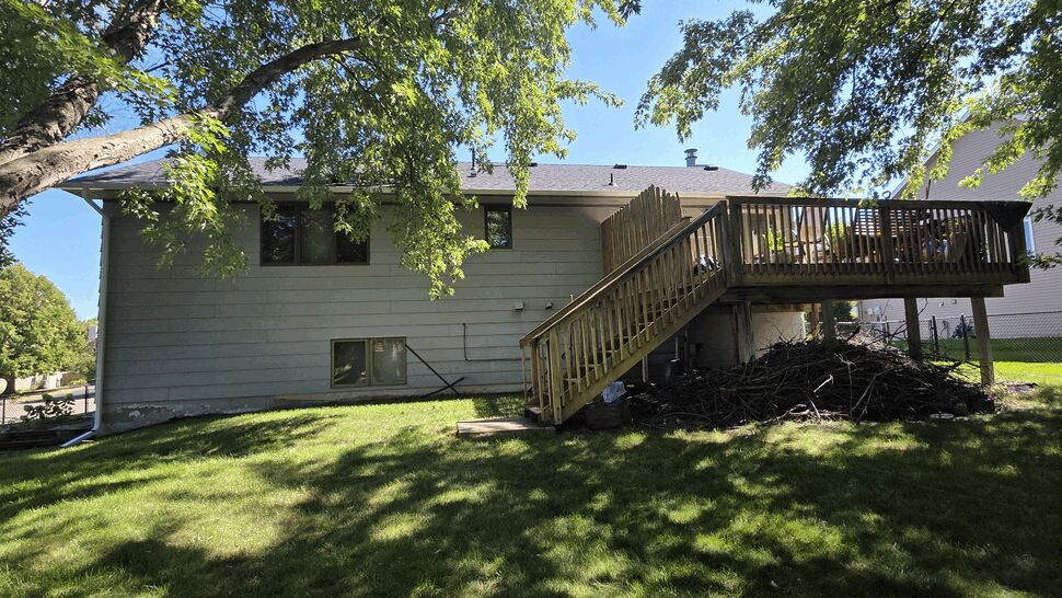 Back of house with an elevated wooden deck, stairs, and shaded backyard.