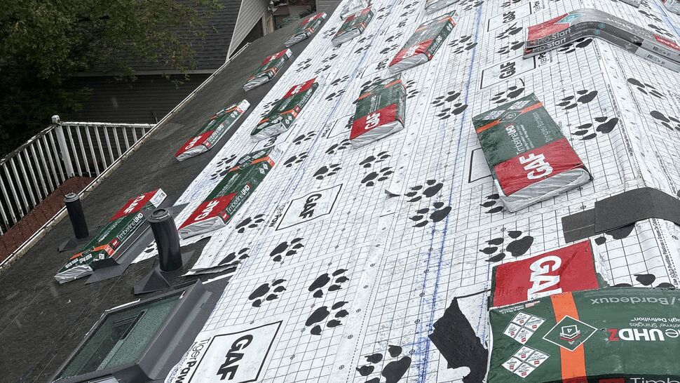 Roof prep with GAF shingle stacks | Lutgen Companies Bundles of GAF Timberline UHDZ shingles and Seal-A-Ridge staged on a roof covered in GAF TigerPaw underlayment and a new Velux Skylight