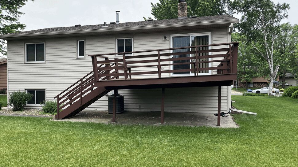 Aging brown-painted wood deck with horizontal railing on a raised ranch home in St. Cloud, MN