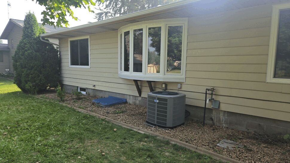 Side of house featuring beige siding and a bay window in summer