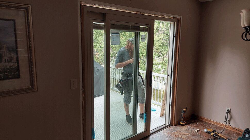 Contractor stands on deck installing a sliding glass patio door.