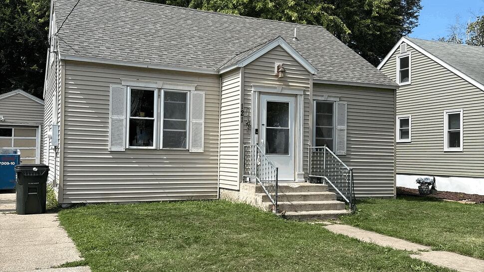 Front view of bungalow with new roof | Lutgen Companies Beige bungalow front with gray shingled roof and concrete walkway.