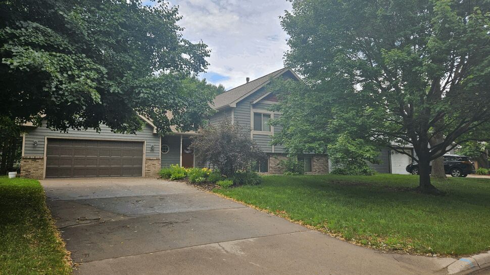 Suburban split-level home with gray siding, attached garage, and large trees.