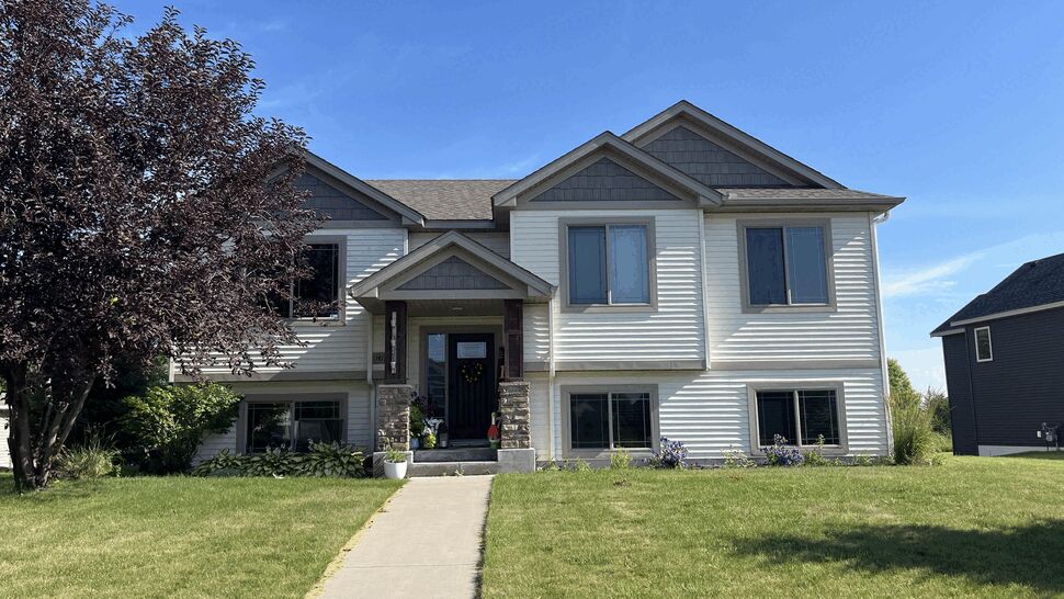 Sunlit front elevation with white siding | Lutgen Companies Front view of white two-story home with lawn and concrete walkway
