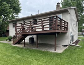 Aging brown-painted wood deck with horizontal railing on a raised ranch home in St. Cloud, MN