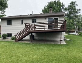 Aging brown-painted wood deck with horizontal railing on a raised ranch home in St. Cloud, MN