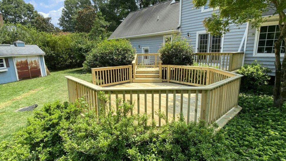 New treated lumber deck with stairs and wood railings beside a gray house