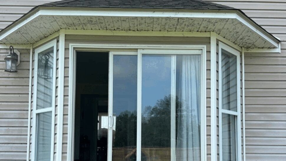 Bay sliding glass door with visible moisture barrier and small hip roof above