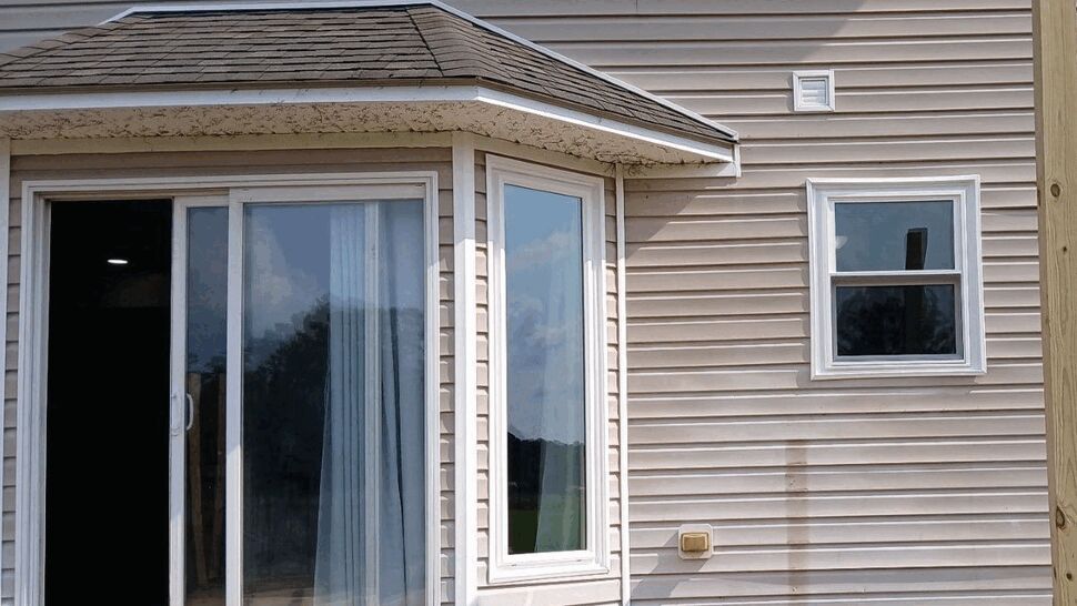 Sliding glass door and bay window set in beige vinyl siding under a small roof