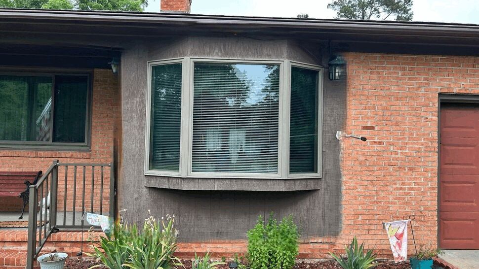 Bay window set in brick with a small flowerbed and porch railing