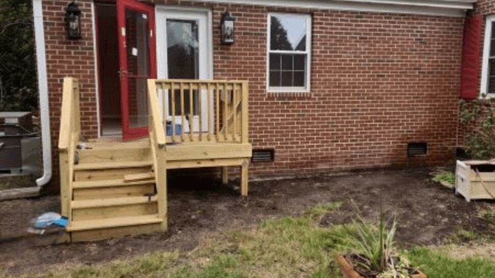 Brick home with gray roof, red entry door, and small wooden deck