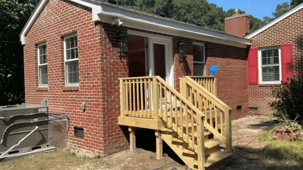 Brick home with a raised wood deck, stairs, entry door, and white gutters