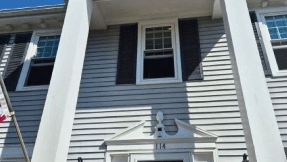 Colonial home entrance with white columns, gray siding, windows, and a black door.