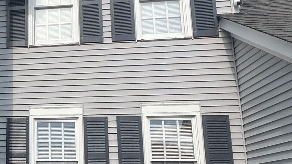 Colonial home exterior with four white windows, dark shutters, gray siding, and white trim.