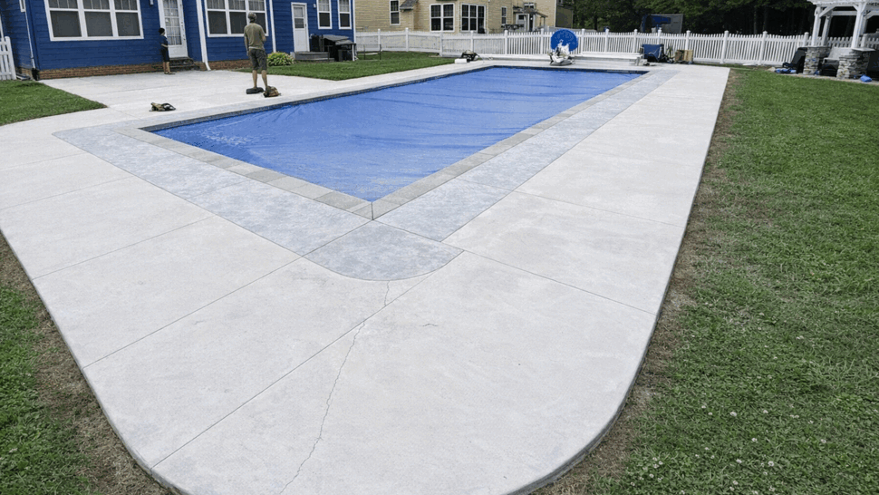 Curved concrete pool deck with blue pool cover and surrounding grass