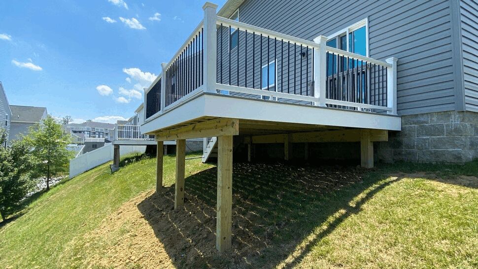 Underside of elevated deck showing white fascia, treated lumber posts and black balusters over sloped yard