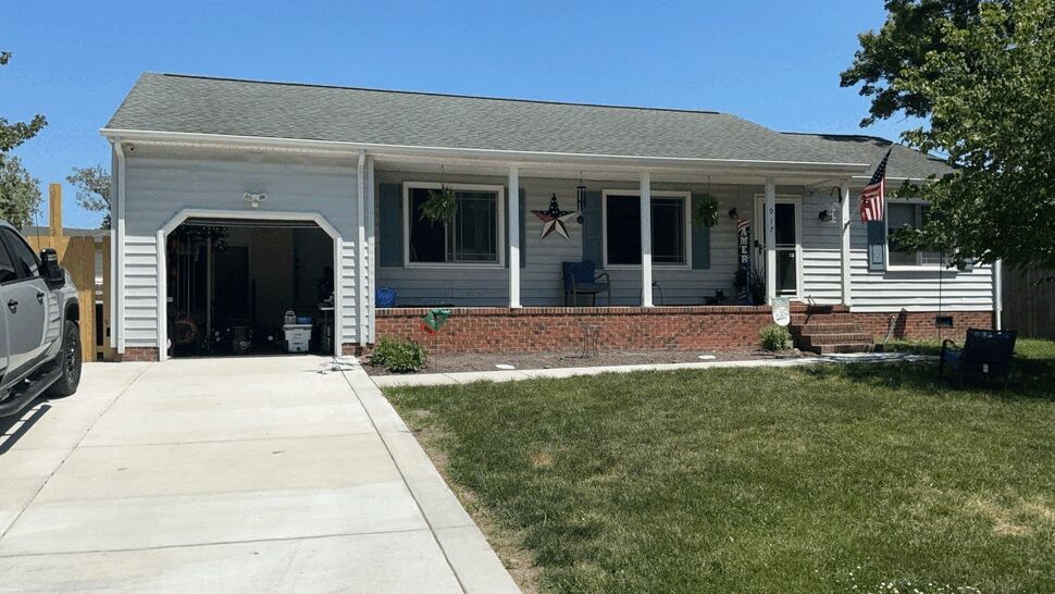Single-story house front with new concrete driveway, porch, and light gray siding.