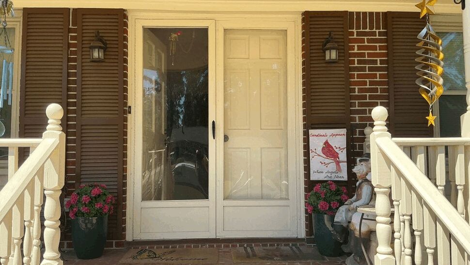 Full front porch with glass storm door, brown shutters, railings and potted flowers