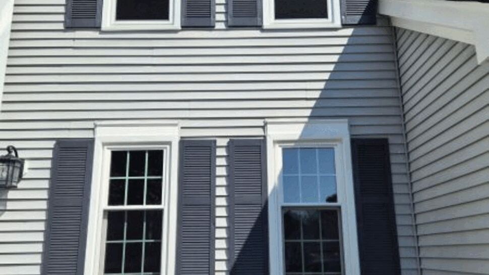Gray-sided home wall with four white-framed windows and dark shutters.