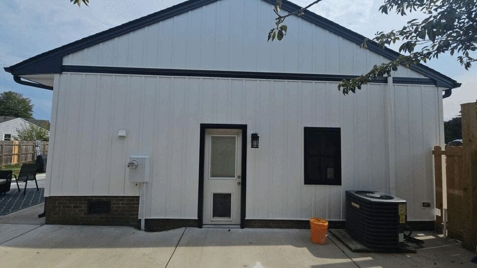 Rear gable wall with white vertical siding, black trim, and newly installed black gutters.