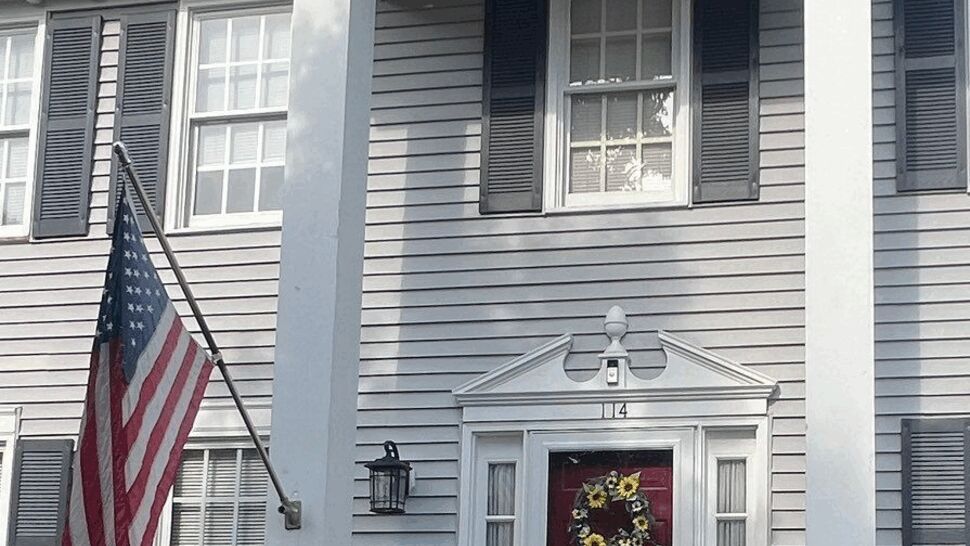 Colonial home with red front door, white columns, gray siding, and brick steps.