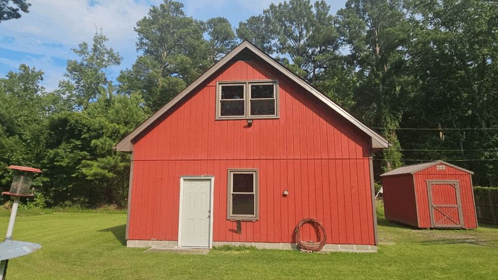 Red two-story outbuilding with a white door and a matching small red shed in the yard