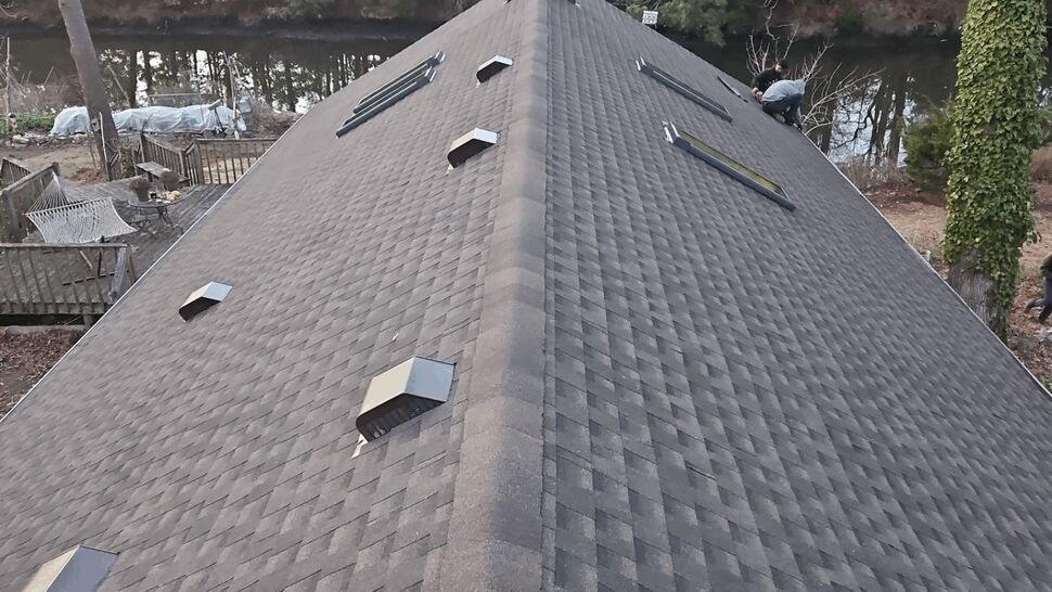 Aerial view of gray asphalt shingle roof with ridge vents and skylights by a river