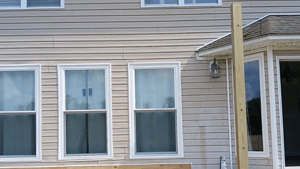 Three vertical single-hung windows on beige vinyl siding with deck posts nearby