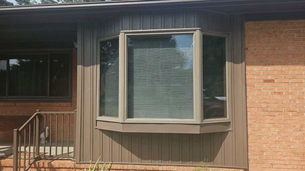 Bay window framed by new vertical brown siding against brick exterior